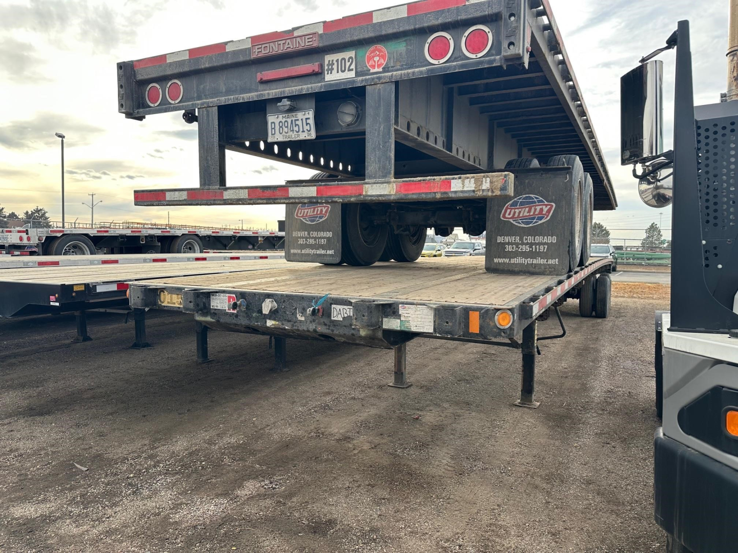 Flatbed trailer with rear ramps from Fontaine Velocity showing dual rear wheels and reflective tape; stock and VIN labels visible on side.