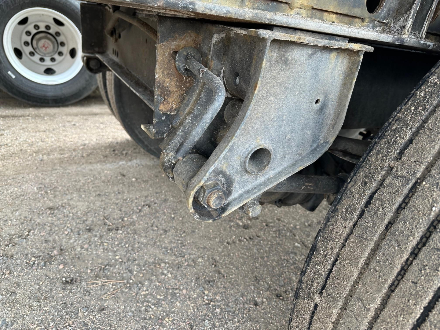Trailer hitch and suspension components on a Fontaine Velocity flatbed trailer showing a steel mounting bracket and a portion of the dual wheels.