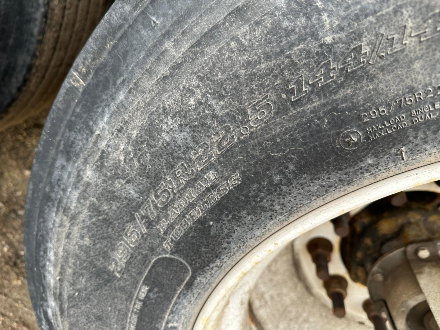 Tractor-trailer tire and hub showing wheel markings including tire size and load rating text.