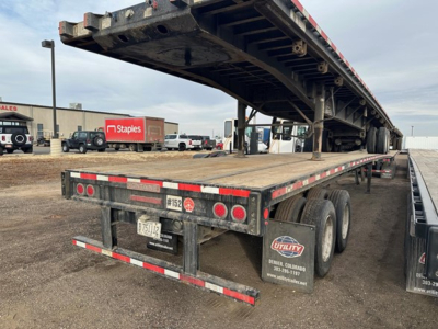 Flatbed trailer in-service with hydraulic lift in open yard showing rear and side ramps and lighting.