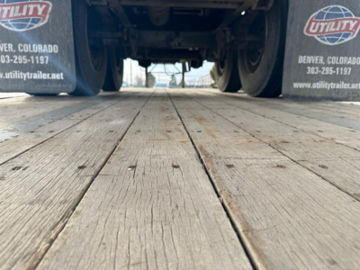 Trailer landing gear and rear deck of a 2018 Fontaine Velocity Steel Flatbed trailer showing wooden deck planks and dual rear tires with Utility trailer logos on mudflaps.