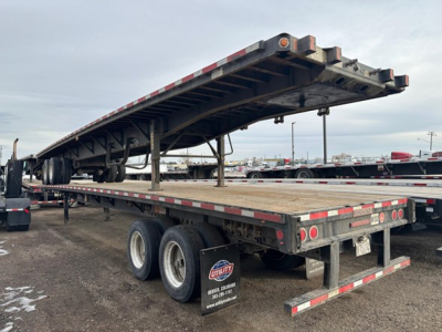 Flatbed trailer showing a raised steel deck on a Fontaine Velocity trailer; rear wheels visible, reflective safety stripes, and tandem axle setup under the deck.
