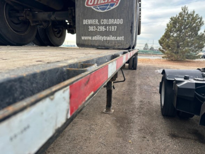 Flatbed trailer edge with reflective side rails and landing gear; Fontaine Velocity branding on fender with Denver, Colorado contact; gravel ground.
