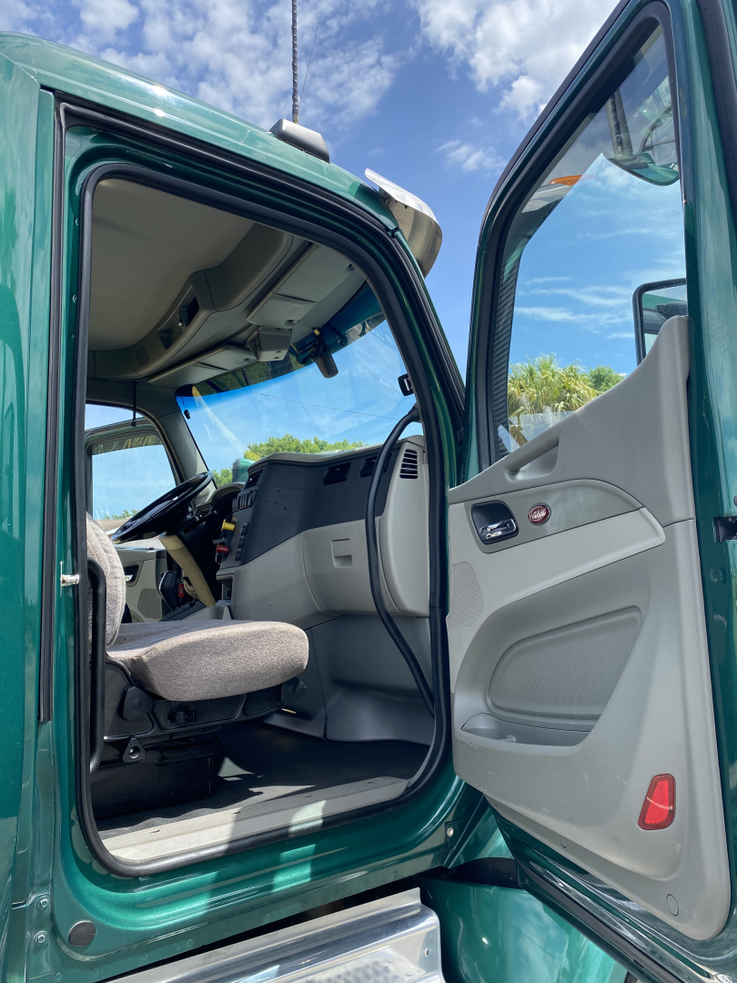  cab interior of a green Peterbilt 579, open driver door, steering wheel and dashboard visible, light gray interior panels.