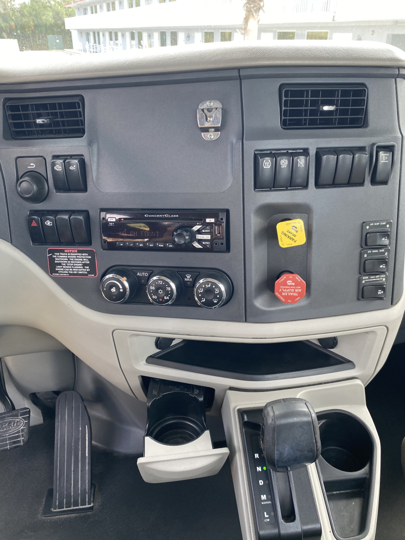 Peterbilt 579 dashboard view showing steering wheel, climate controls, CD/Radio, power switches, and cup holder area.