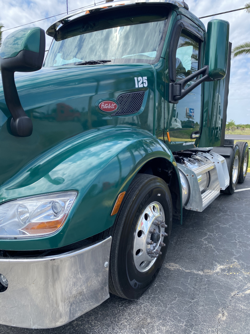 Peterbilt 579 daytime cab truck in teal/green with hood number 125, front fender, side mirror, and dual rear wheels visible