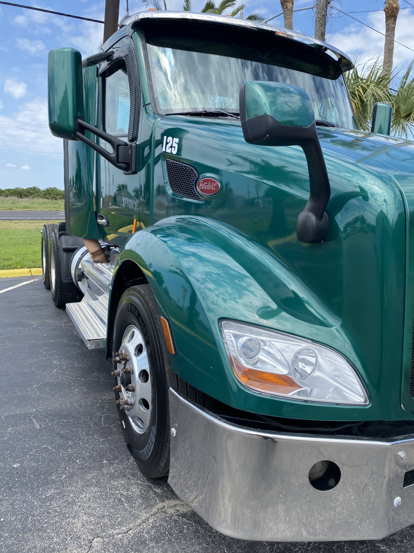 Peterbilt 579 daytime cab front-side view showing green exterior, charcoal mirrors, chrome bumper, headlight assembly, and model badge 125 on fender.