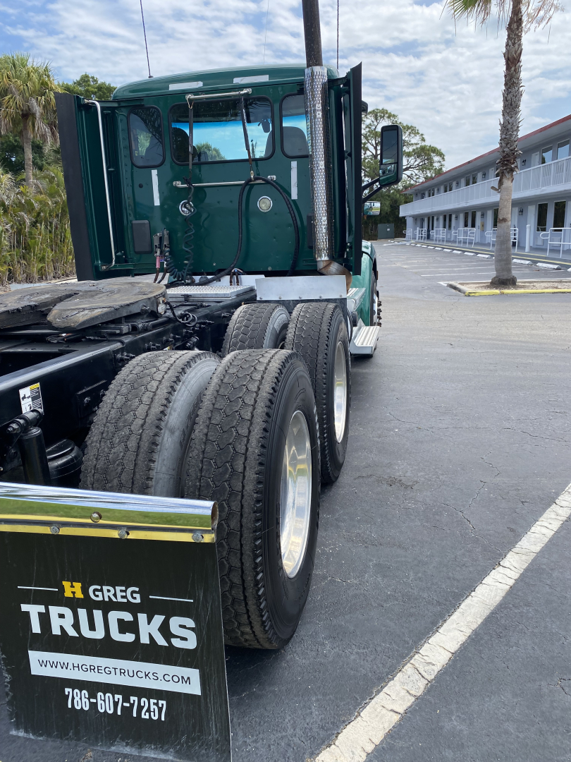 Peterbilt 579 truck rear-side view with dual rear axles and green cab, shows branding on mud flap and tires.
