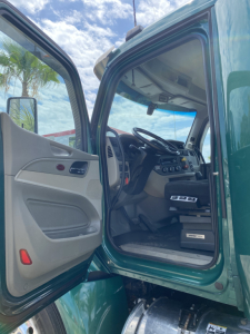 Truck cab interior of a 2018 Peterbilt 579 with open driver door, showing steering wheel, dashboard, and entry area.