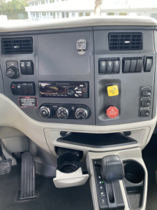 Peterbilt 579 dashboard view showing steering wheel, climate controls, CD/Radio, power switches, and cup holder area.