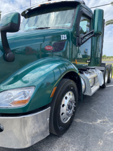 Peterbilt 579 daytime cab truck in teal/green with hood number 125, front fender, side mirror, and dual rear wheels visible