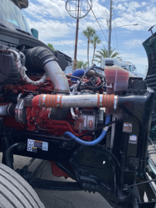 Peterbilt 579 engine bay showing Cummins/engine components with hoses and coolant reservoir visible.