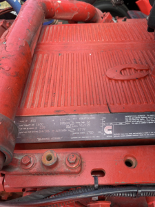 Peterbilt 579 engine bay with red-painted components and identification plate showing specifications and VIN area.
