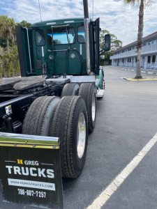 Peterbilt 579 truck rear-side view with dual rear axles and green cab, shows branding on mud flap and tires.