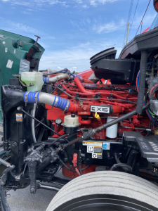 Peterbilt 579 engine bay with red engine block labeled X15 showing hoses, coolant reservoir, and surrounding components