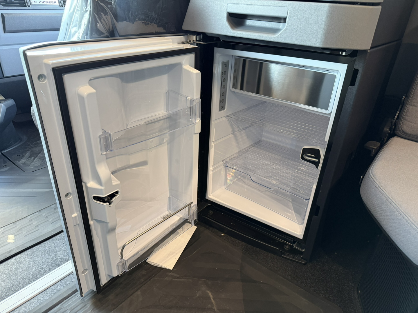 Fridge unit in a 2027 Mack PR64T76H cab showing open compact refrigerator with freezer shelf and interior compartments.