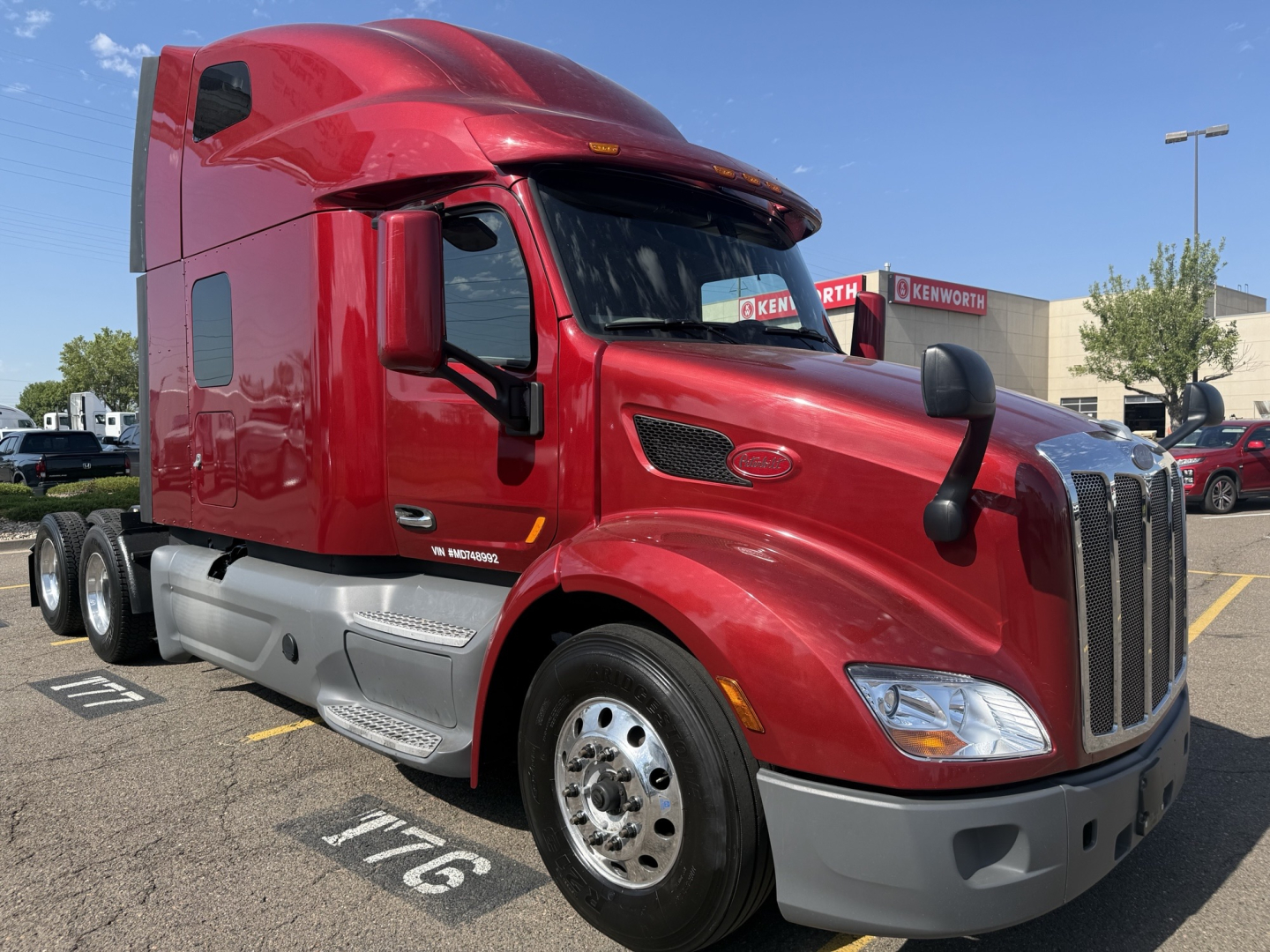 Red Peterbilt 579 truck in a parking lot showing cab and front wheel with chrome rims; visible text includes badges and model details on the side and bumper.