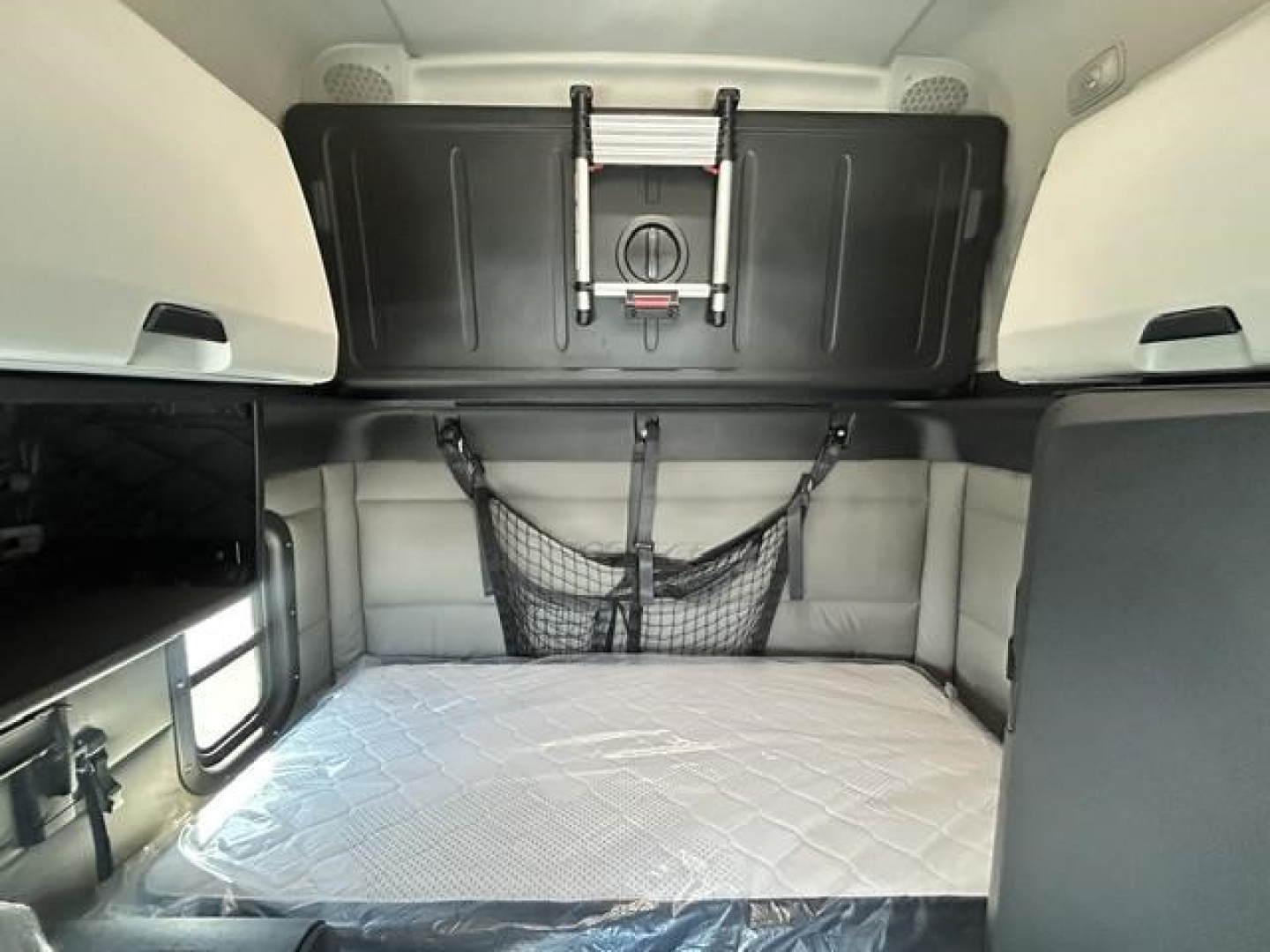 Cascadia sleeper cab interior with bed mattress, storage nets, and overhead cabinets.