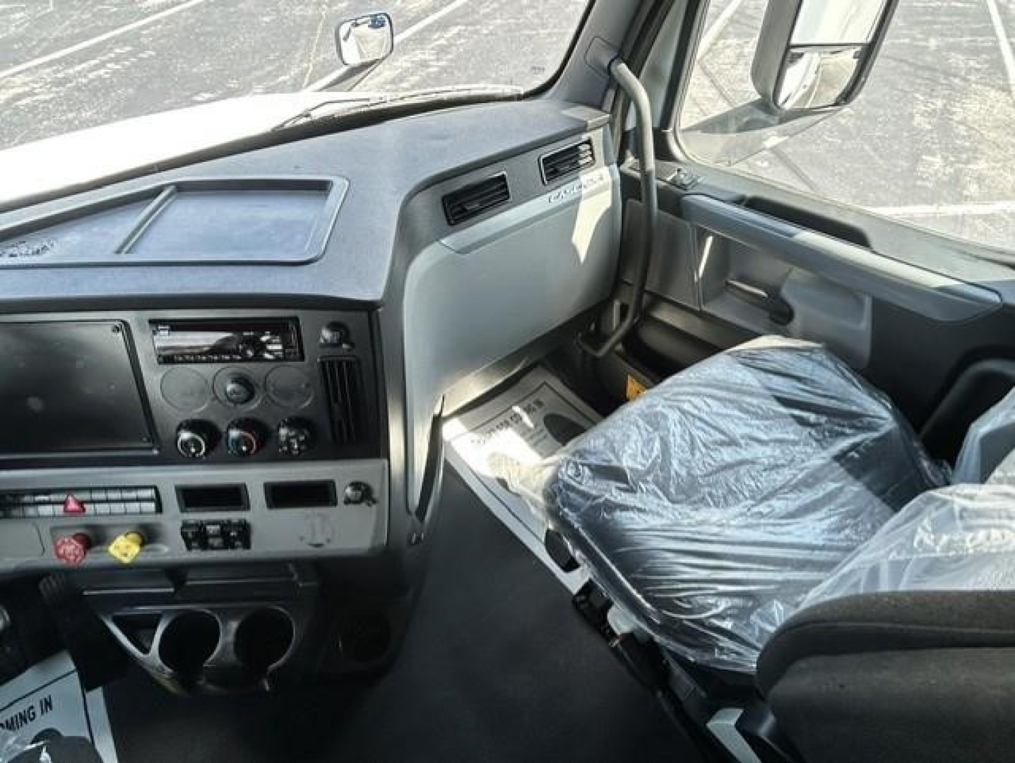 Cab interior of a Freightliner Cascadia 126 truck showing steering wheel, dashboard, and plastic-covered driver seat.