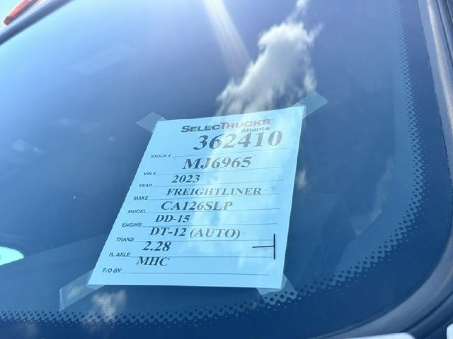 Vehicle window sticker visible on the dashboard showing 2023 Freightliner Cascadia DD-15 DT-12 (AUTO) 2.28 MHC, CA126SLP, stock 362410, VIN MJ6965.
