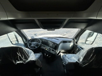 Truck cab interior of a 2021 Freightliner Cascadia 126 showing steering wheel, dashboard, and two front seats covered in plastic.