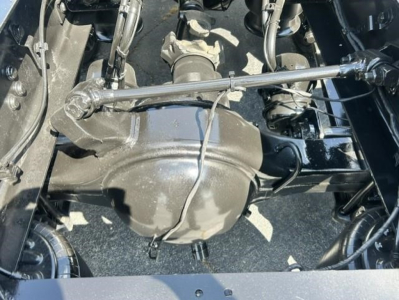 Truck drivetrain center with differential housing and suspension components visible under Freightliner Cascadia chassis, transmission linkage and hoses in view.