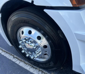 Truck wheel close-up showing chrome hubcap and Bridgestone tire on a Freightliner Cascadia 126 front fender. Visible wheel cover and part of white truck body.