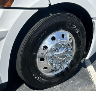 Truck wheel and tire on a 2021 Freightliner Cascadia 126; chrome hubcap with visible lug nuts; tire sidewall shows Bridgestone or Goodyear branding and tread pattern; white truck body panel nearby.