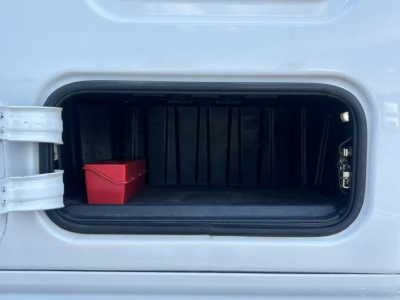 Trunk/storage compartment of a Freightliner Cascadia shows empty storage bay with a small red bin and latch hardware.