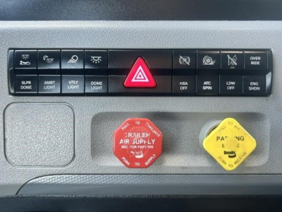 Dashboard panel of a Freightliner Cascadia 126 showing hazard light switch, auxiliary controls, red engine air supply knob, and yellow dipper/cover for fluid access.