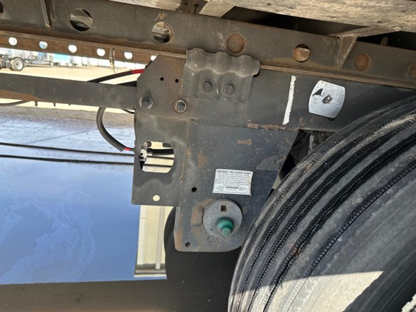 Truck trailer level view showing frame, mounting bracket, and coiled electrical connector near wheel on a 2021 Utility 3000R reefer trailer.