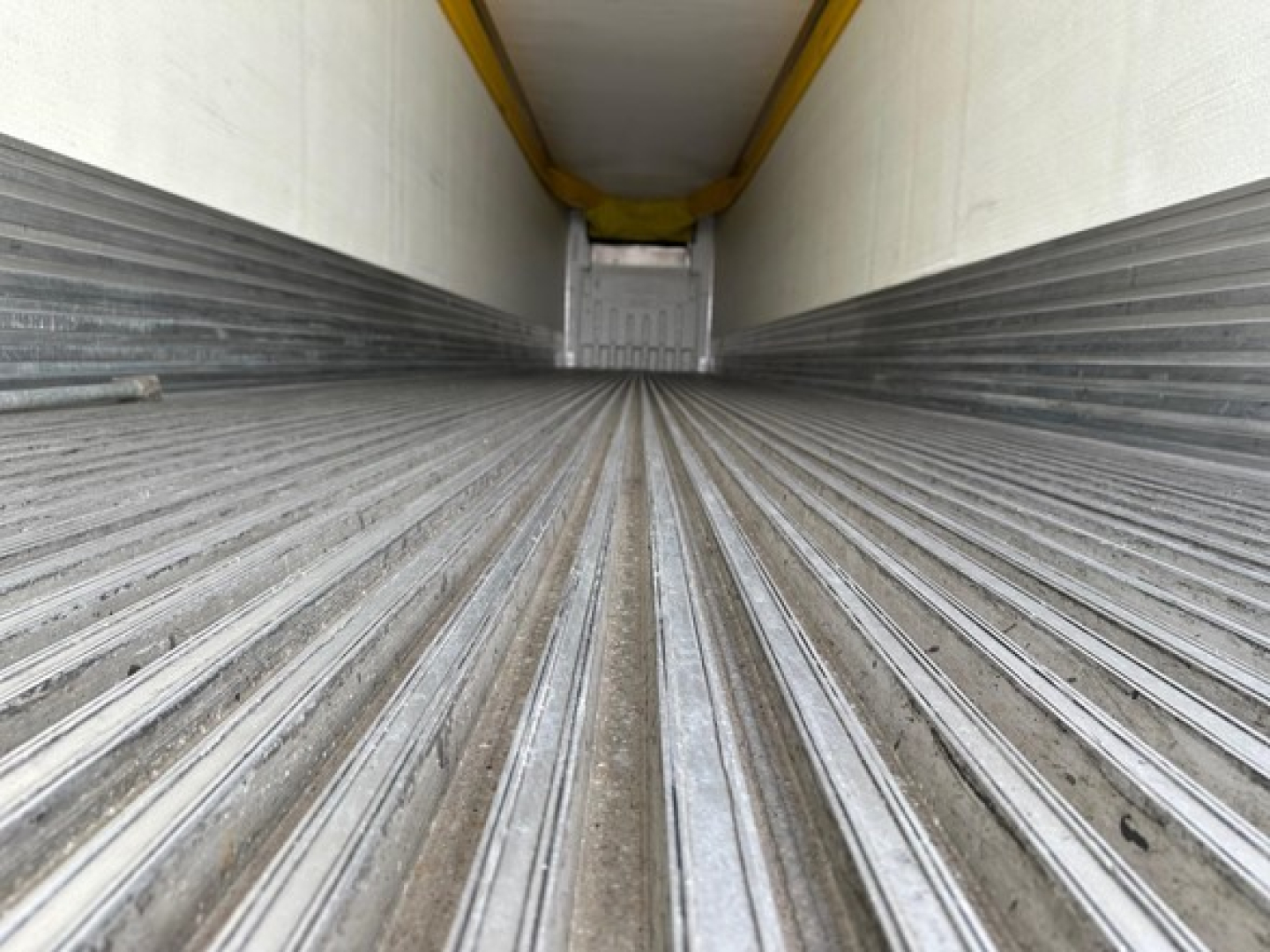 Trailer interior showing ribbed metal floor and side walls of a refrigerated trailer with a white ceiling and yellow contact mechanisms.