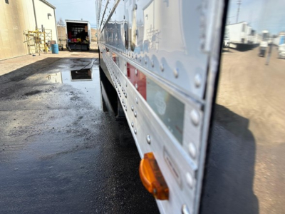 Trailer side view with reflective aluminum panels and orange side marker light. Visible rivets and door seam along the utility reefer trailer.