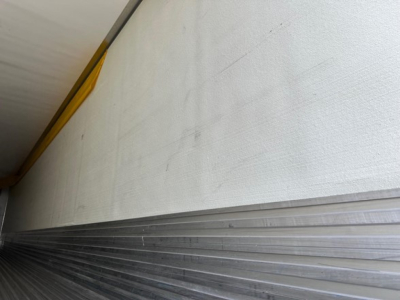 Trailer side showing smooth white wall with ribbed aluminum lower edge and a small yellow safety reflector, no legible text.