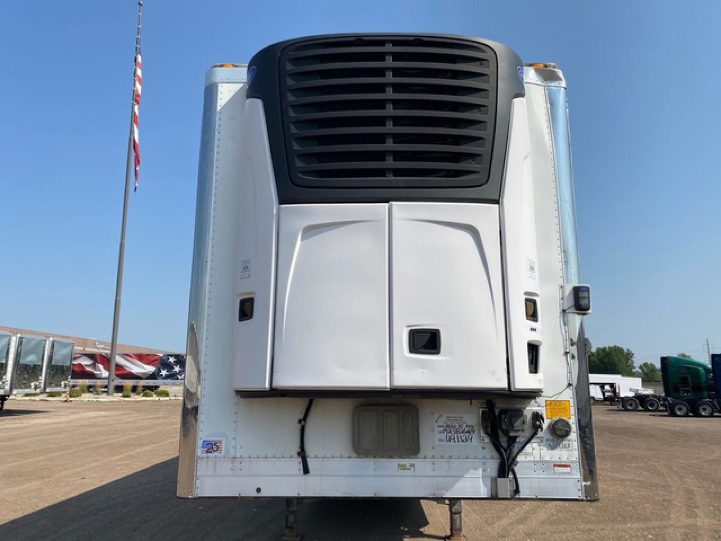 Rear view of a 2021 utility reefer trailer showing refrigerator unit and back doors with wiring harness and bumper.