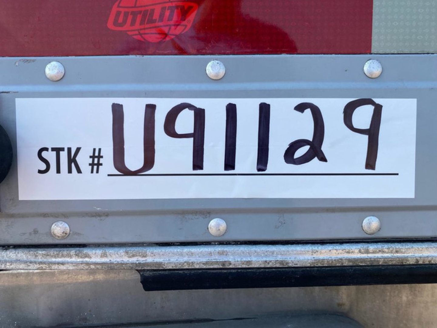Trailer stock tag reading STK # U911129 with large handwritten U91129 on white label, mounted on silver metal with rivets.