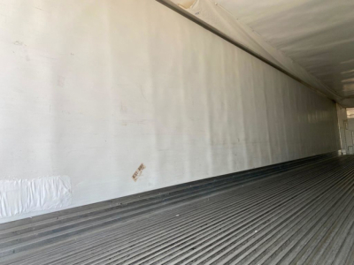 Container trailer interior with corrugated metal floor and smooth white sidewall, empty cargo bay.