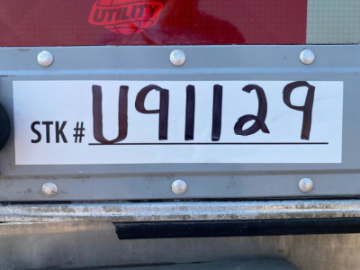 Trailer stock tag reading STK # U911129 with large handwritten U91129 on white label, mounted on silver metal with rivets.