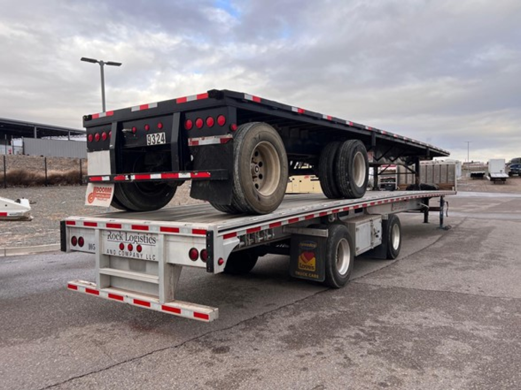 Rear and side view of a Mac All Aluminum flatbed trailer on a multi-axle lowboy. Visible text includes parts of license plate and reflective strips.