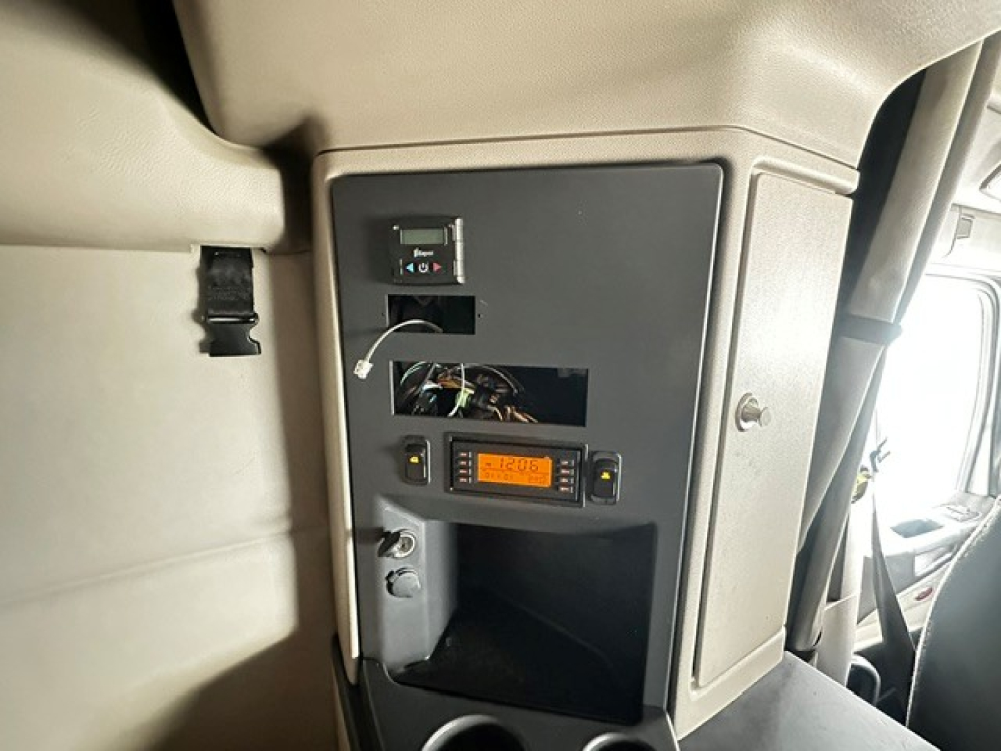 Truck interior dash panel showing diagnostic display and wiring access panel in the cab of a Peterbilt 579 sleeper. LCD display present, wiring exposed, small storage shelf.