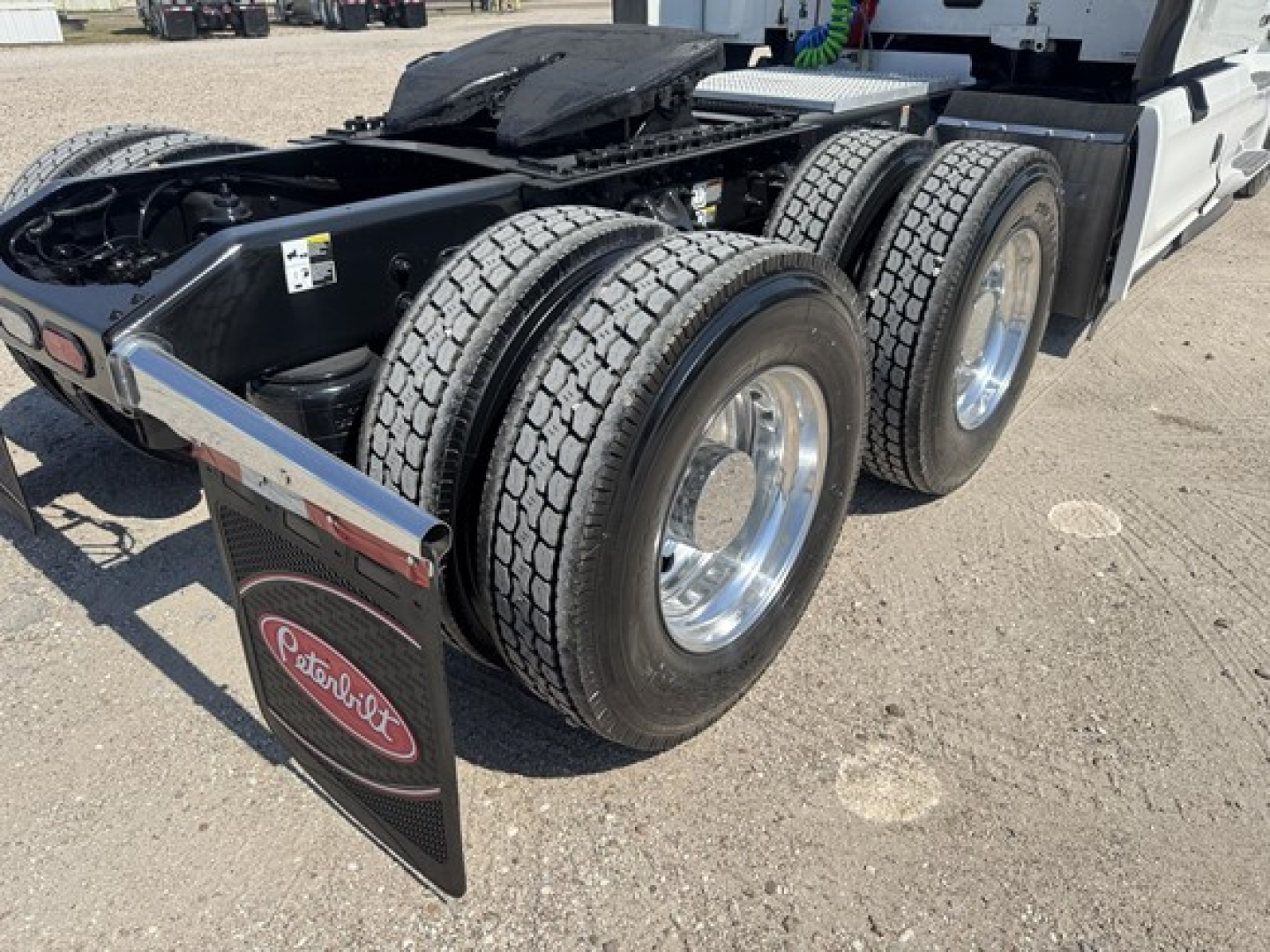 Trailerless rear wheel area of a Peterbilt 579 tractor showing dual rear axles and chrome wheels, bumper mudflap with Peterbilt logo, and fifth wheel mounting plate.