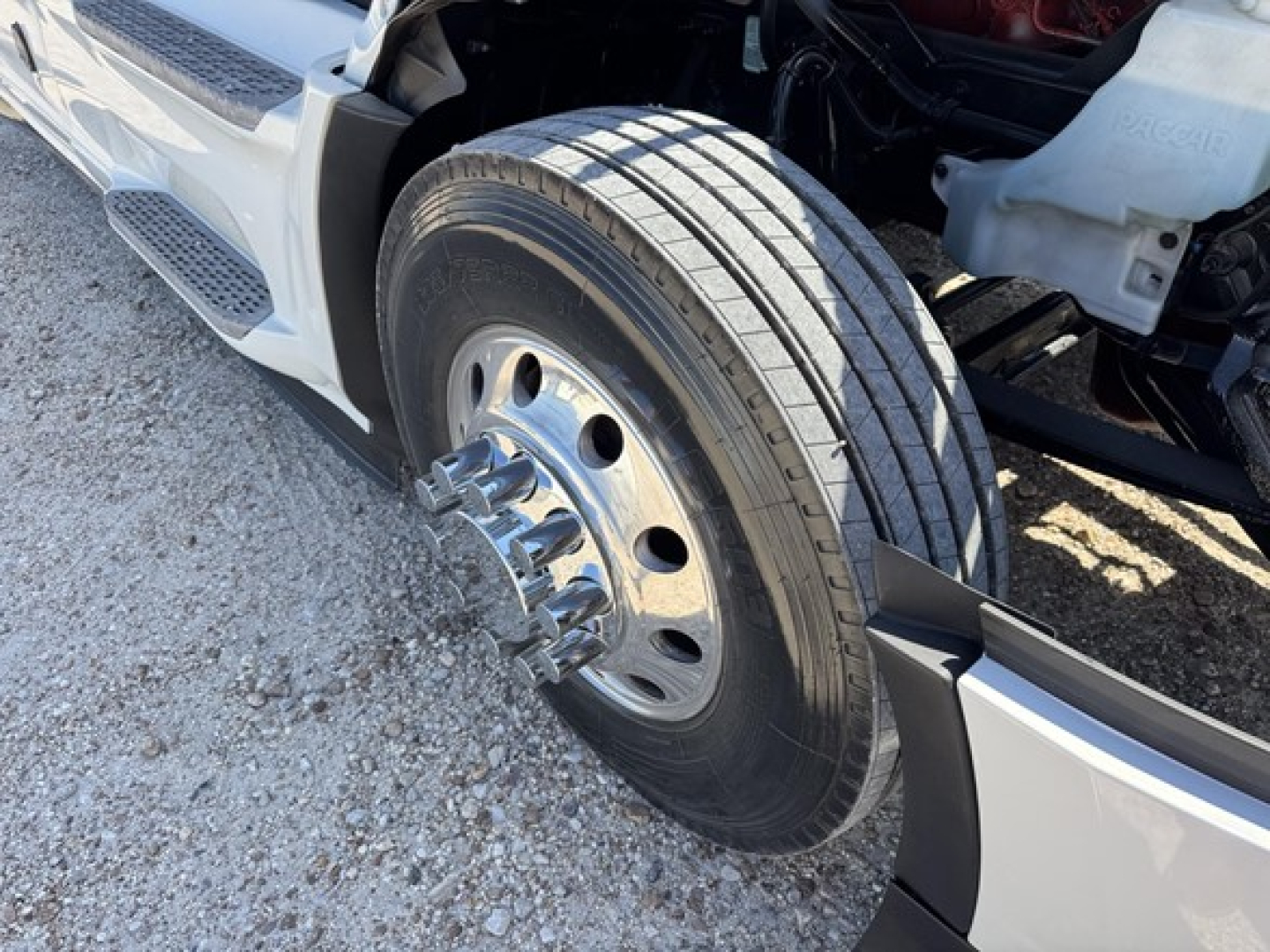 Peterbilt 579 front wheel and tire, hub with lug nuts, partial view of front fender and bumper.