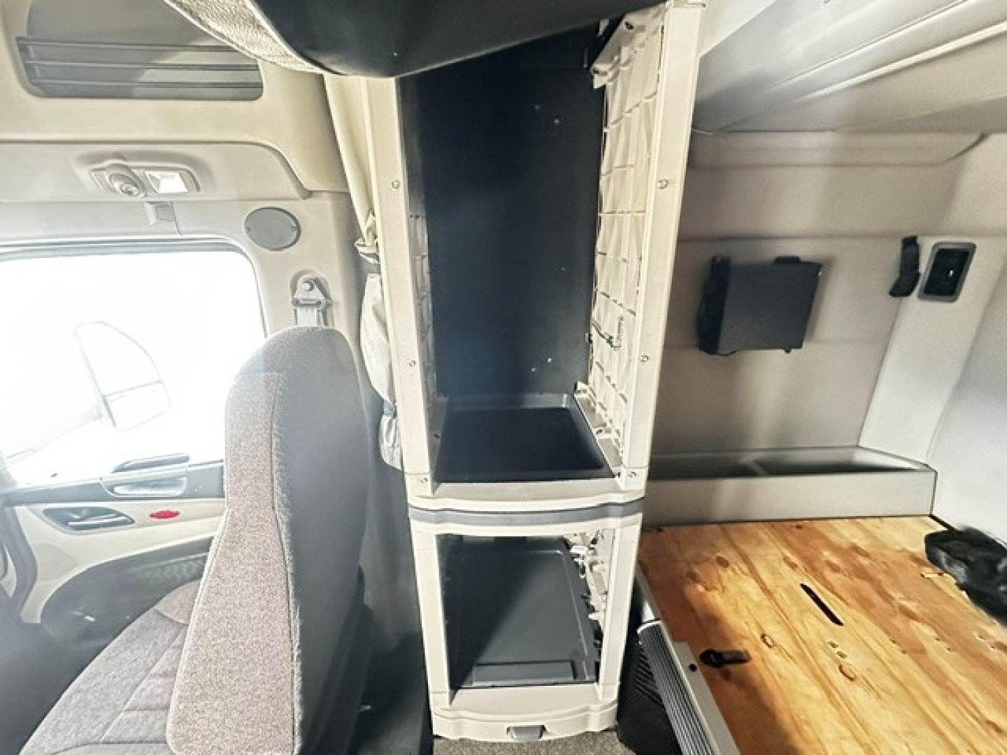 Peterbilt 579 interior center console area with open storage compartments and wooden floor; cab interior visible with driver's seat and dashboard edges.
