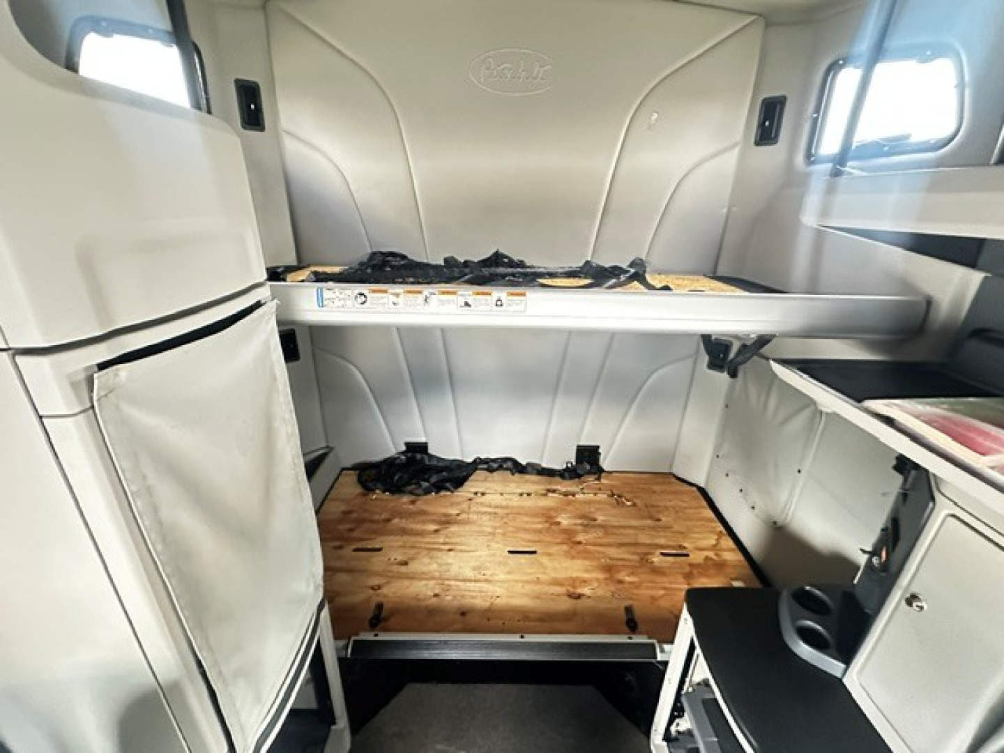 Peterbilt 579 sleeper cab interior showing lower bunk bed area with wood floor and storage cabinets.