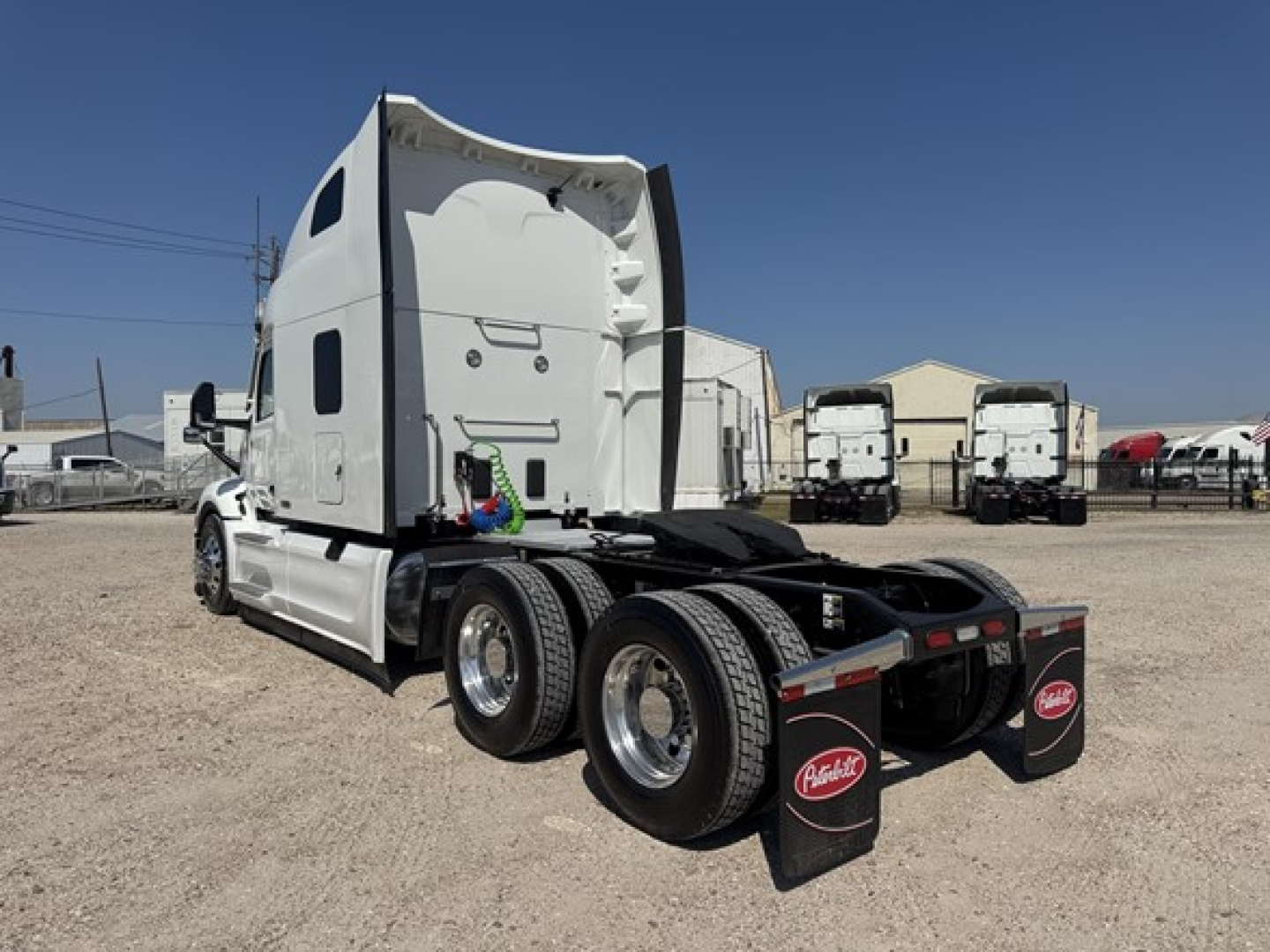 Peterbilt 579 tractor in a lot, rear view showing triple rear axles and chassis, white cab, black fifth wheel area, mudflaps with Peterbilt logo.