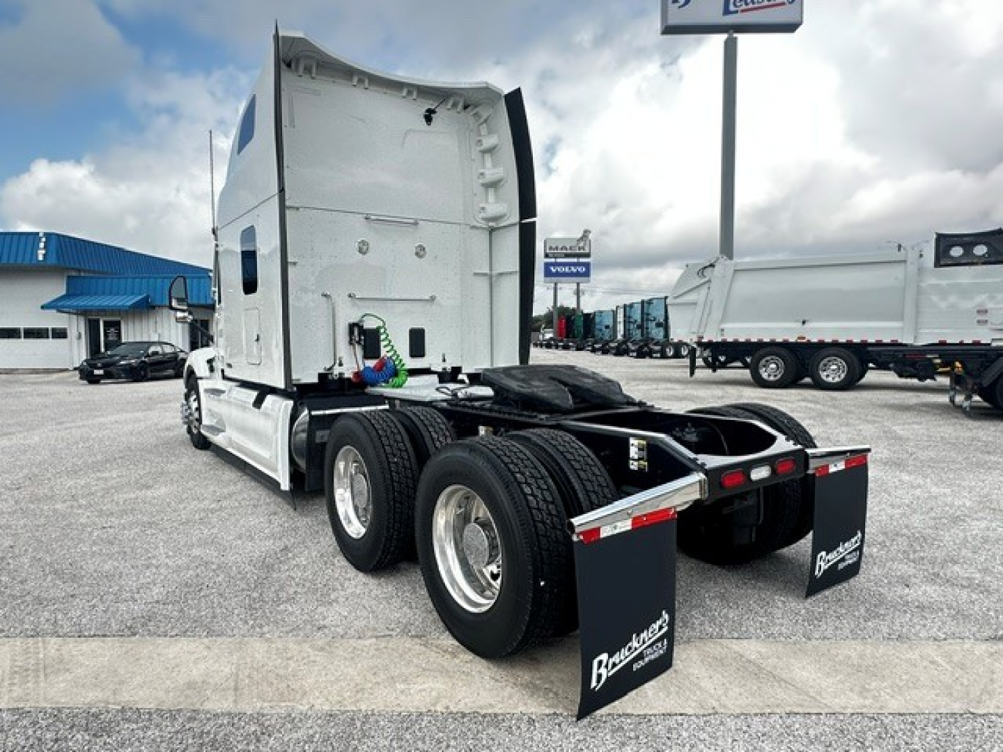 Peterbilt 579 tractor rear view showing dual rear axles with mud flaps, fifth wheel area, and exhaust stack; white cab with sleeper, lots of chrome wheels.