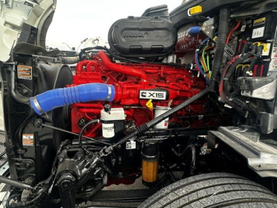 Peterbilt 579 engine bay showing red Cummins engine with blue hose, black air intake cover, and various wiring harnesses.