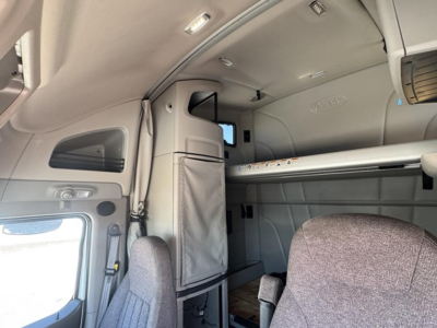 Peterbilt 579 sleeper cab interior showing upper bunk, storage compartments, and dashboard area with light gray upholstery.