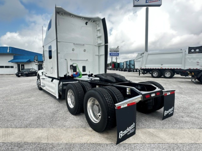 Peterbilt 579 tractor rear view showing dual rear axles with mud flaps, fifth wheel area, and exhaust stack; white cab with sleeper, lots of chrome wheels.