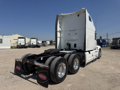 Peterbilt 579 sleeper cab tractor in a used truck lot, rear view showing triple axle configuration and fifth wheel, white cab with black chassis.